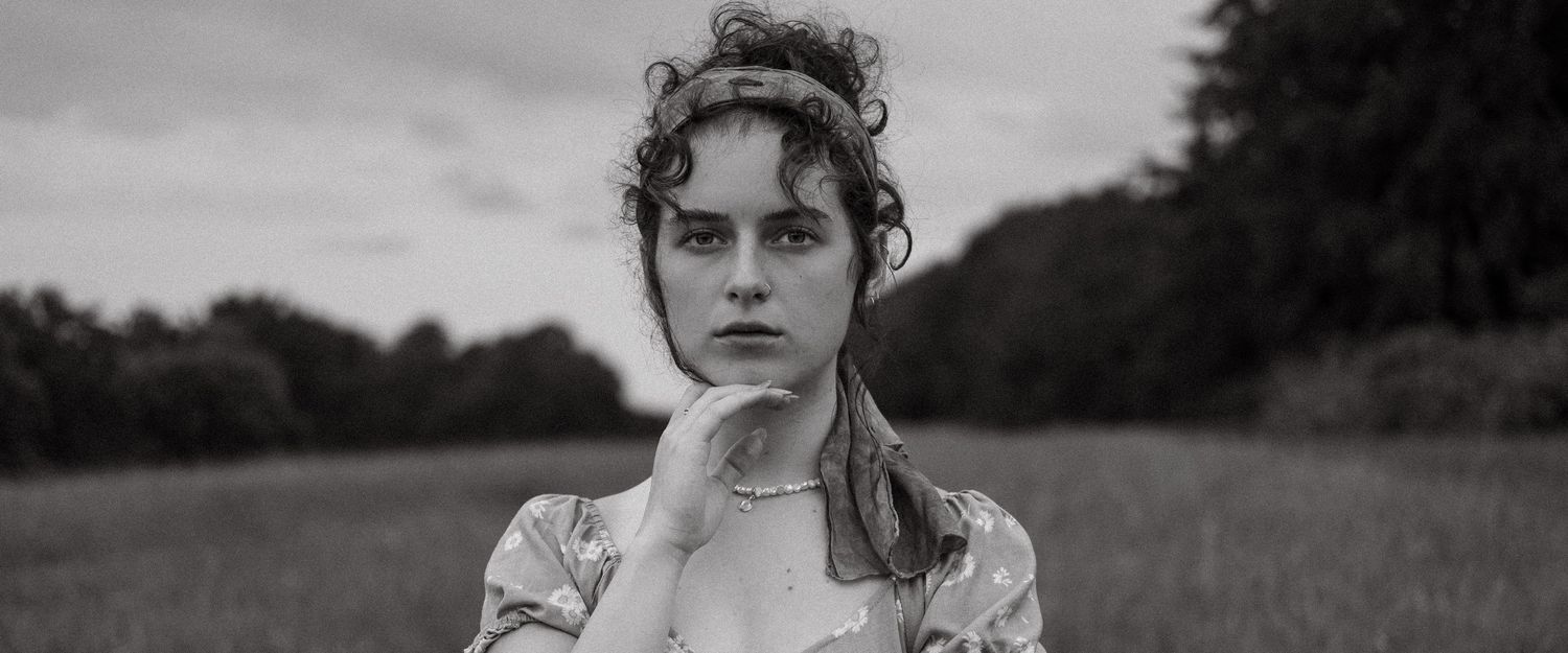 Black and white portrait of a woman standing in a field, photographed in a natural cinematic style.
