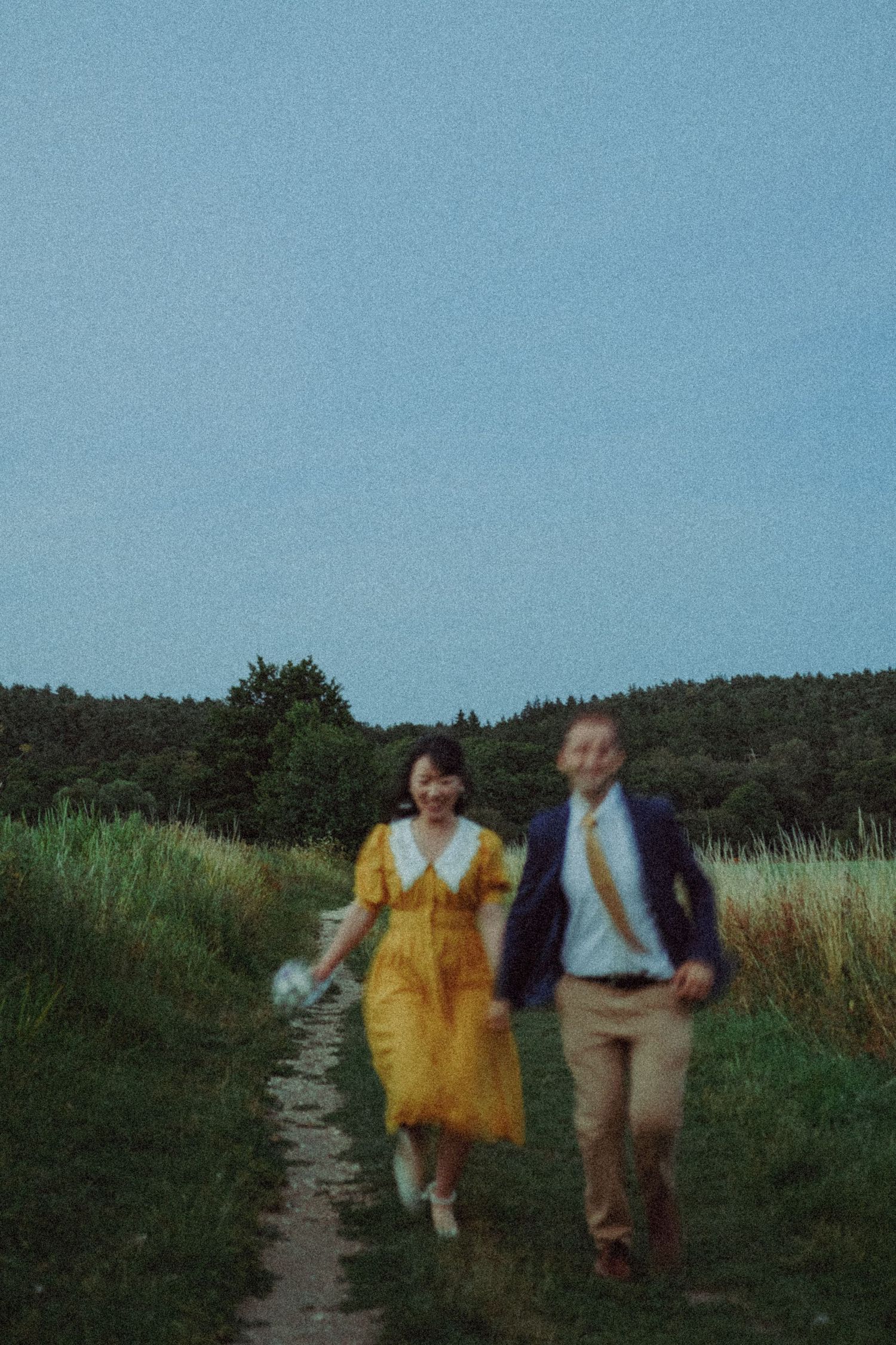 Newlywed couple running in a field for a cinematic photoshoot. Wearing yellow dress