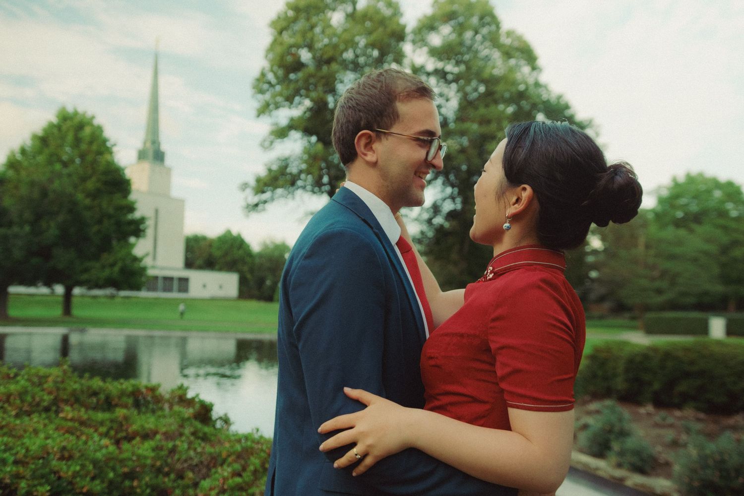 Romantic pre-wedding photograph of a couple embracing beside a lake, in front of church, captured in a natural cinematic style.