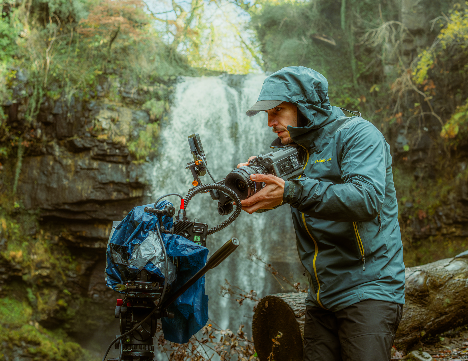 Behind-the-scenes photograph of a cinematographer operating a professional cinema camera on location beside a waterfall.