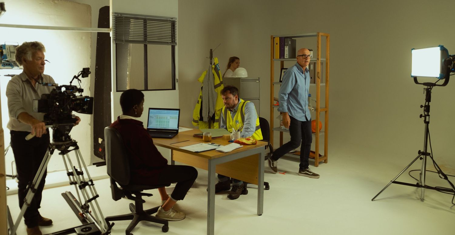 Behind-the-scenes photograph of a commercial film shoot with actors, lighting and production equipment on set.
