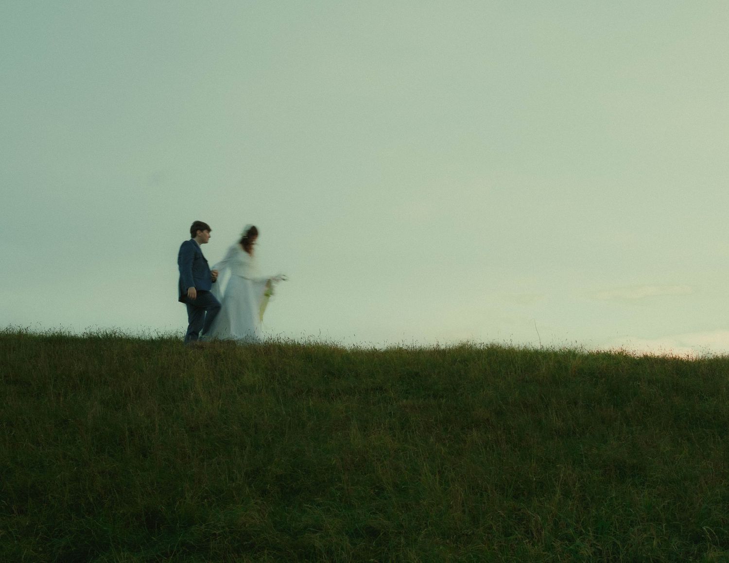 Couple walking together across an open field during a cinematic pre-wedding photoshoot