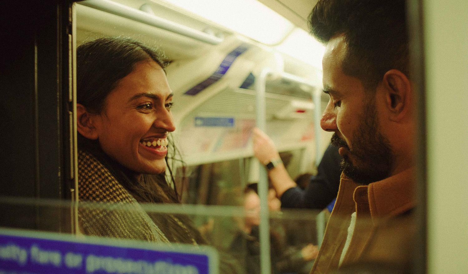 Candid couples photograph of a couple sharing a joyful moment together on a train, captured through the window.