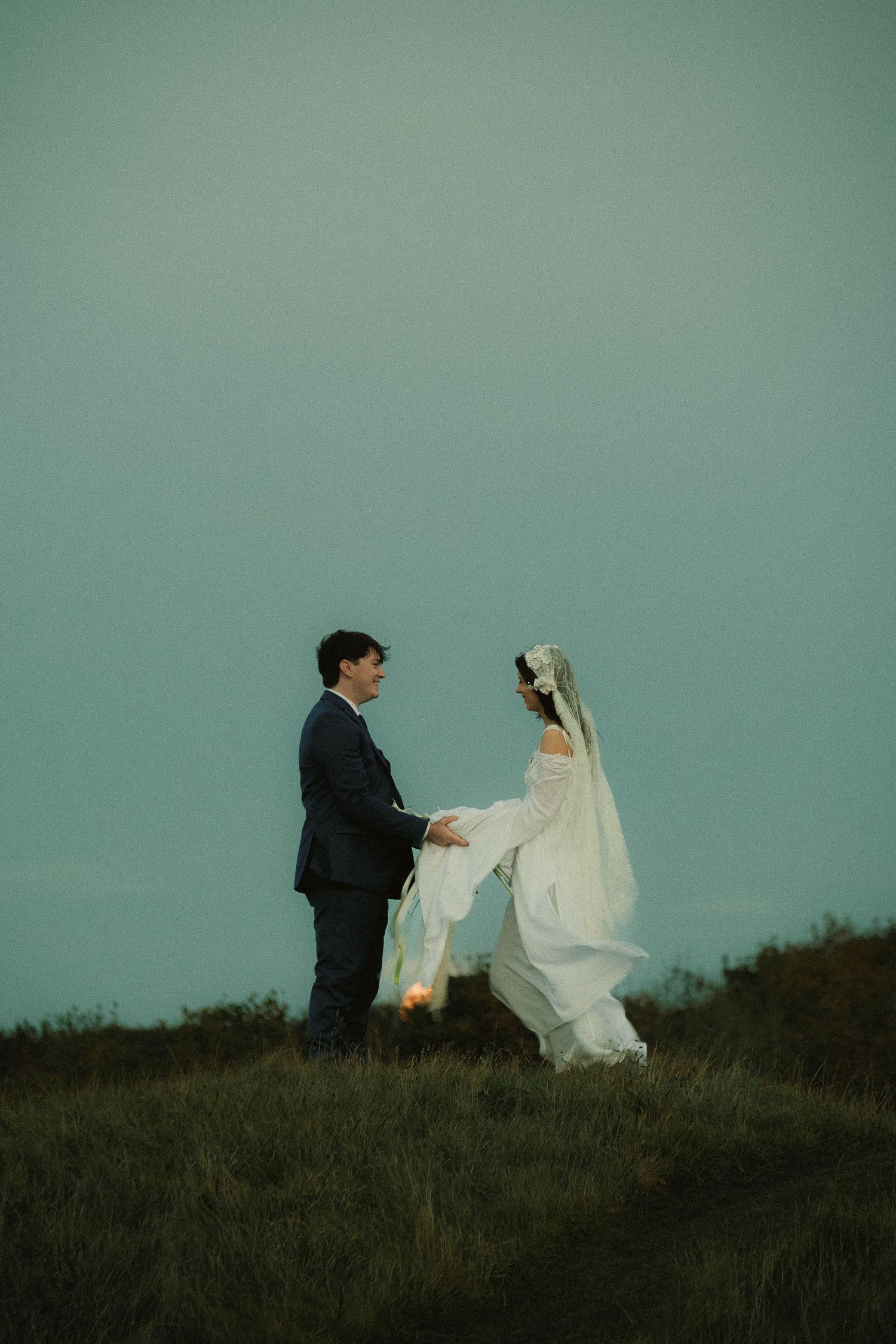 Newlywed couple standing together in an open field during a cinematic wedding photoshoot
