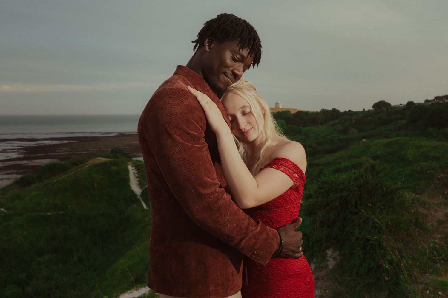 Young couple sharing a moment during a cinematic pre-wedding session on a cliff with an ocean view.