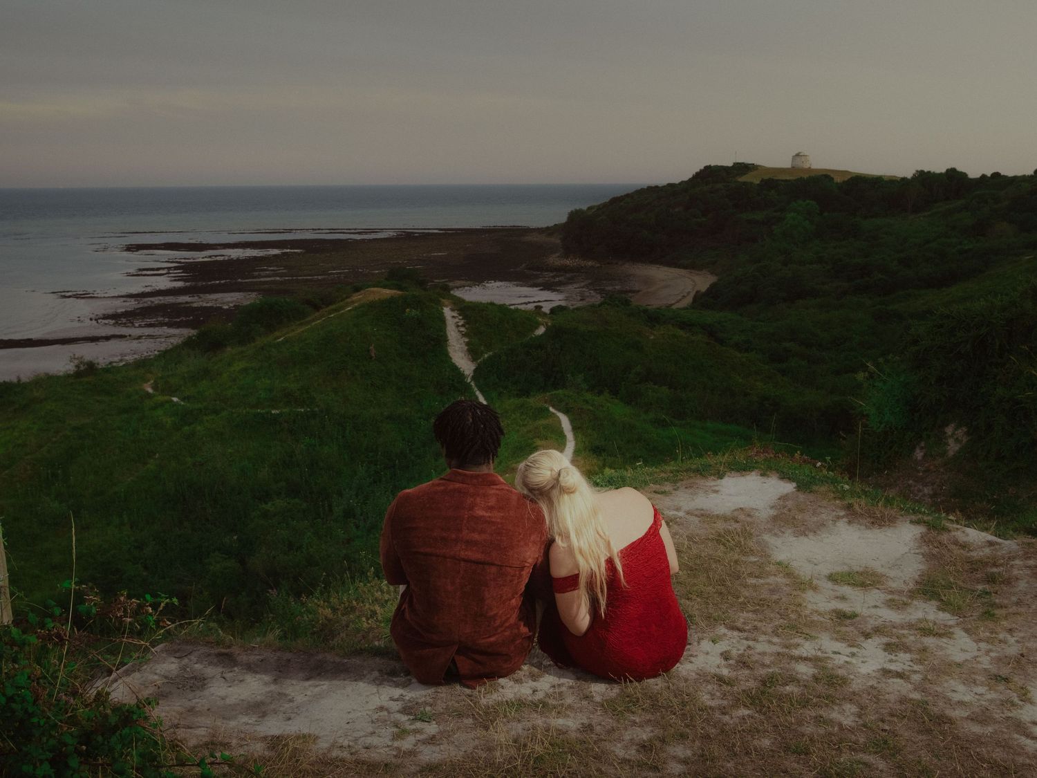 Young couple sharing a moment during a cinematic pre-wedding session on a cliff with an ocean view.