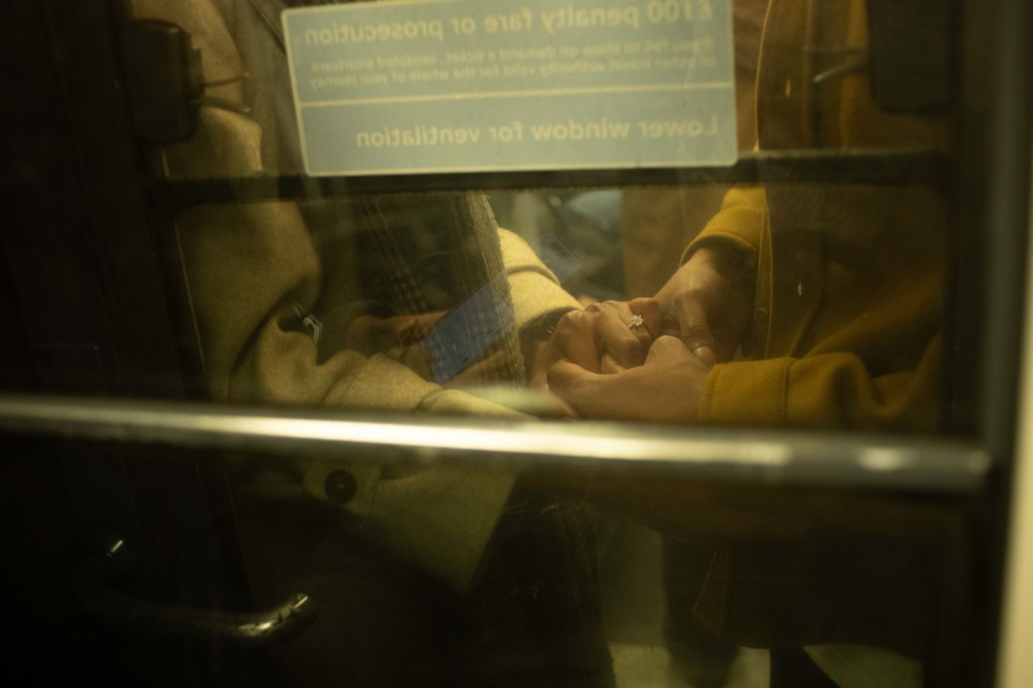 Intimate couples photograph of two people holding hands on a train, captured through the window with a cinematic atmosphere.