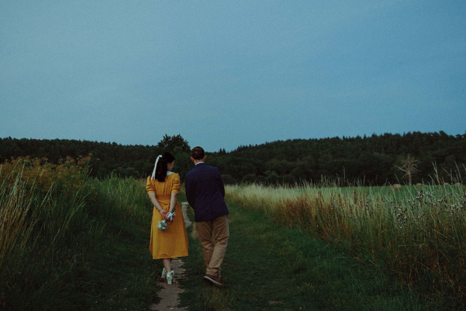 Couple walking together through a field during a cinematic pre-wedding photoshoot