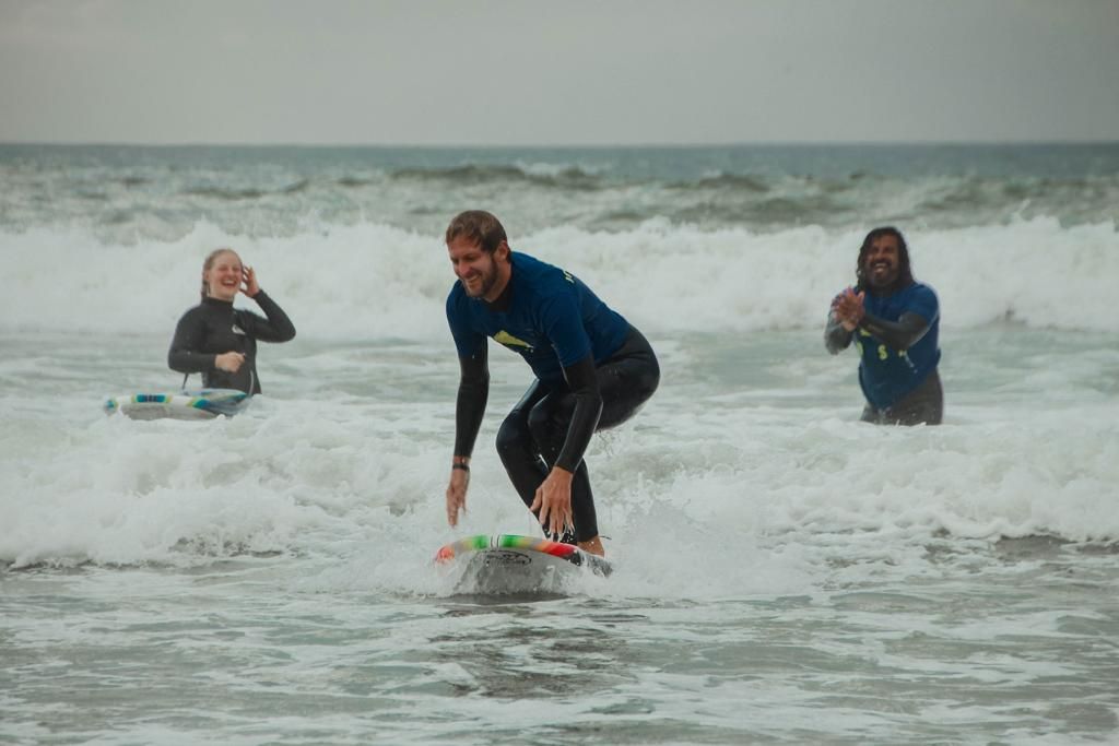 A surfer in a wetsuit rides a wave while two others watch in the ocean background.