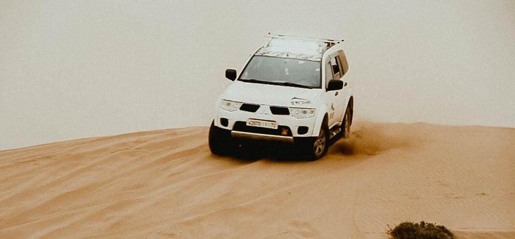 A white 4x4 SUV navigating steep sandy desert dunes in a thrilling off-road adventure under a hazy sky.