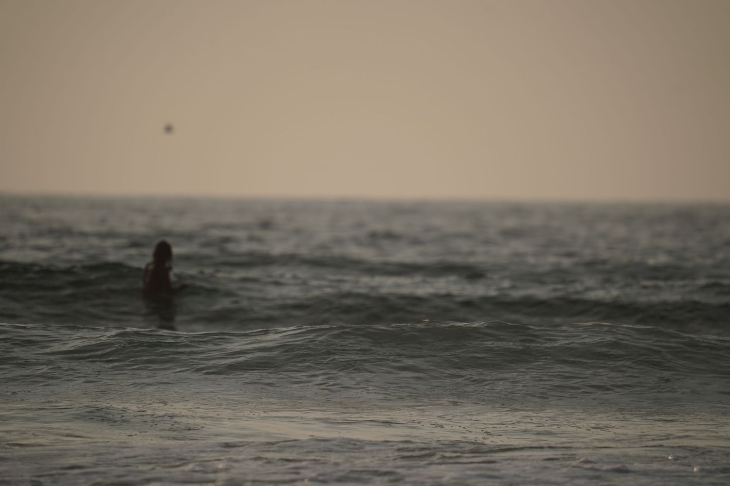A lone swimmer stands waist-deep in ocean waves during golden hour at dusk.