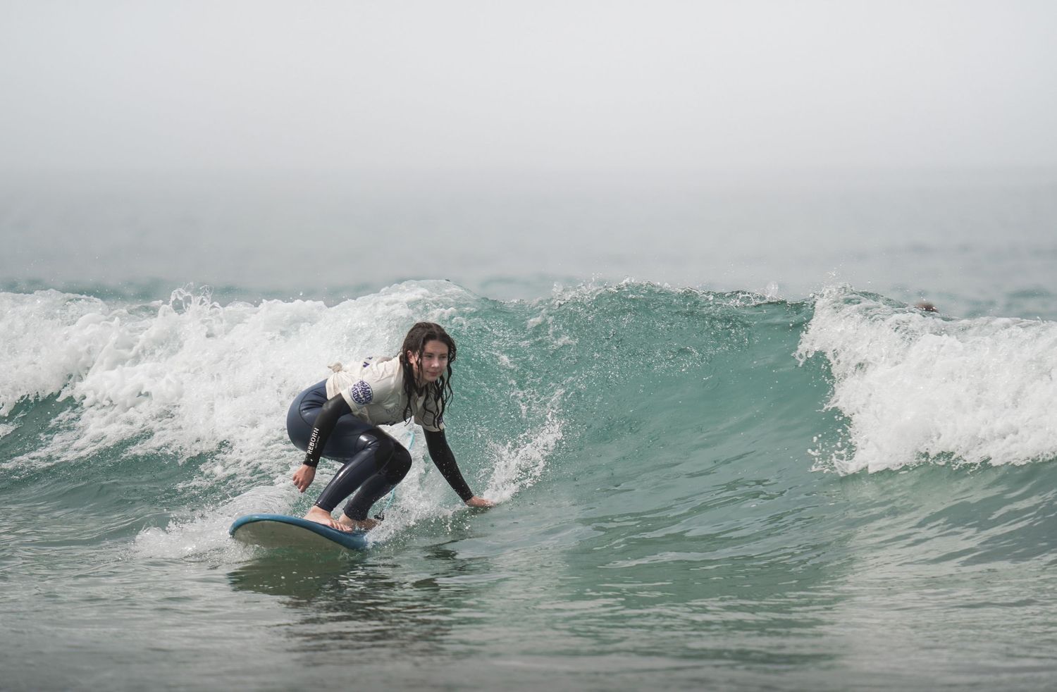 A surfer rides a wave in a wetsuit on a foggy day at the beach.