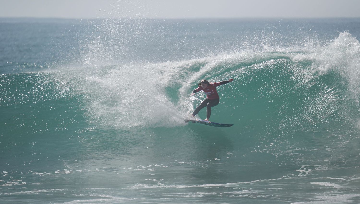 Surfer riding a large green wave during a surfing competition in the ocean.