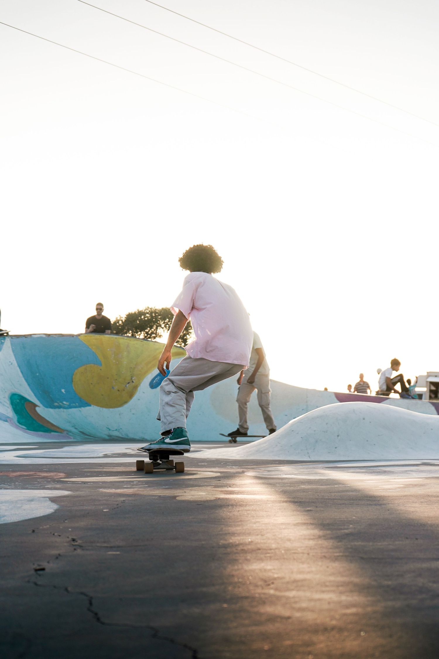 Skateboarder performing tricks on a colorful painted ramp at a sunny outdoor skate park with spectators.
