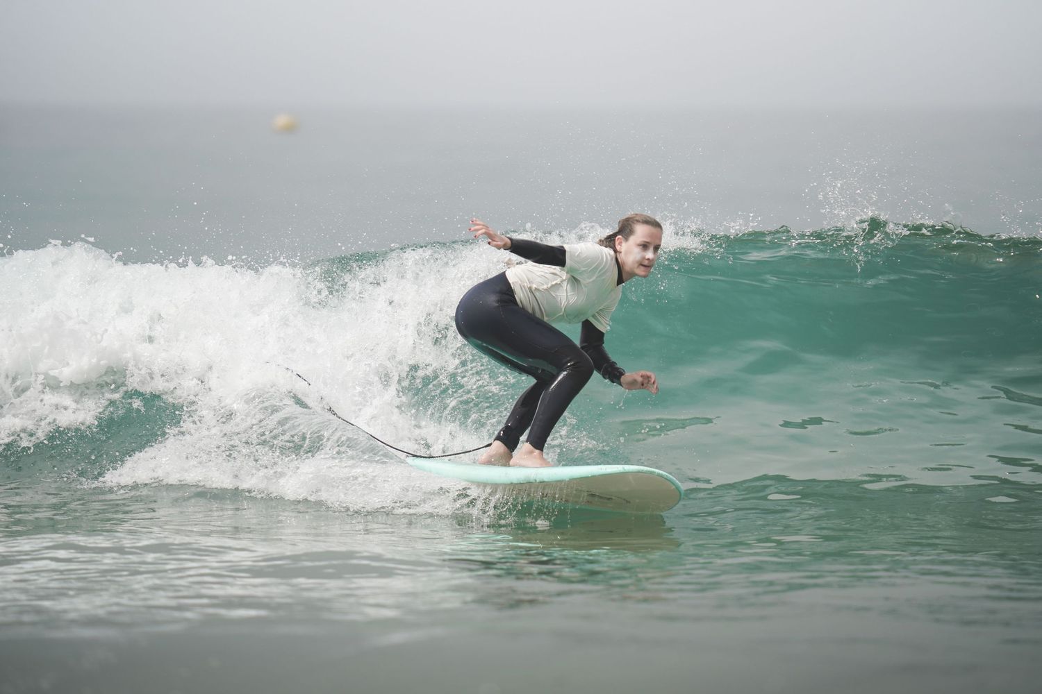 Young woman in wetsuit surfing a wave on a white surfboard in the ocean on a cloudy day.