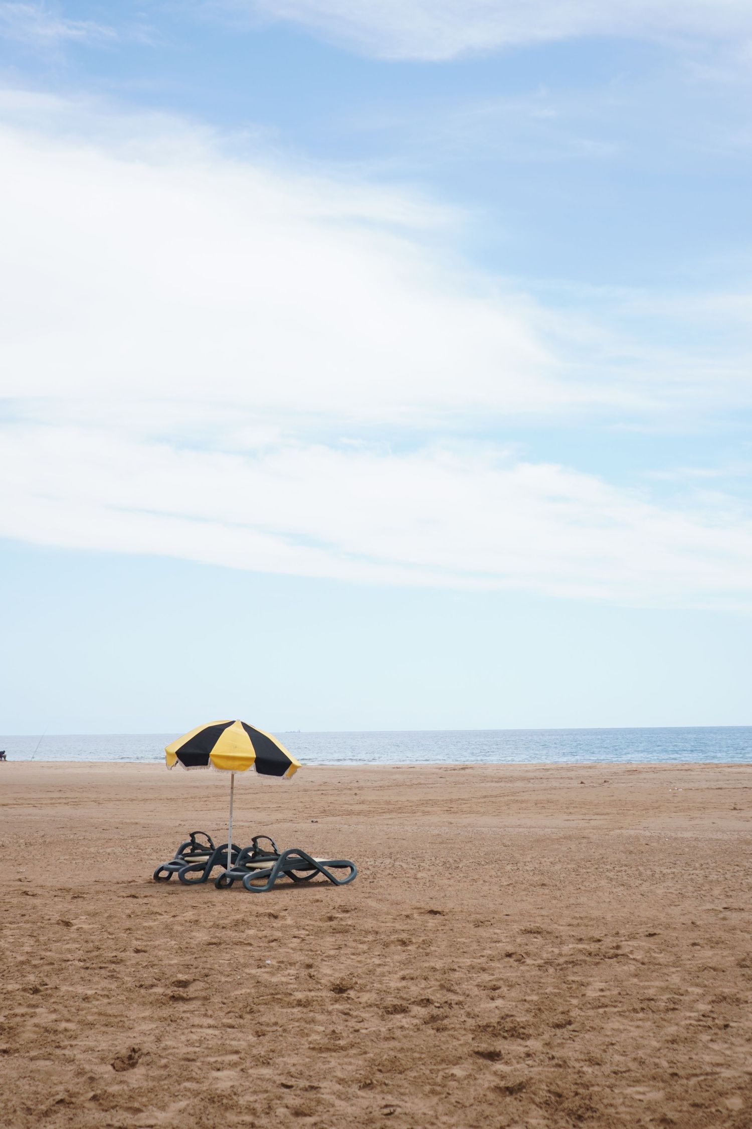 A yellow and black striped beach umbrella with lounge chairs on an empty sandy beach.