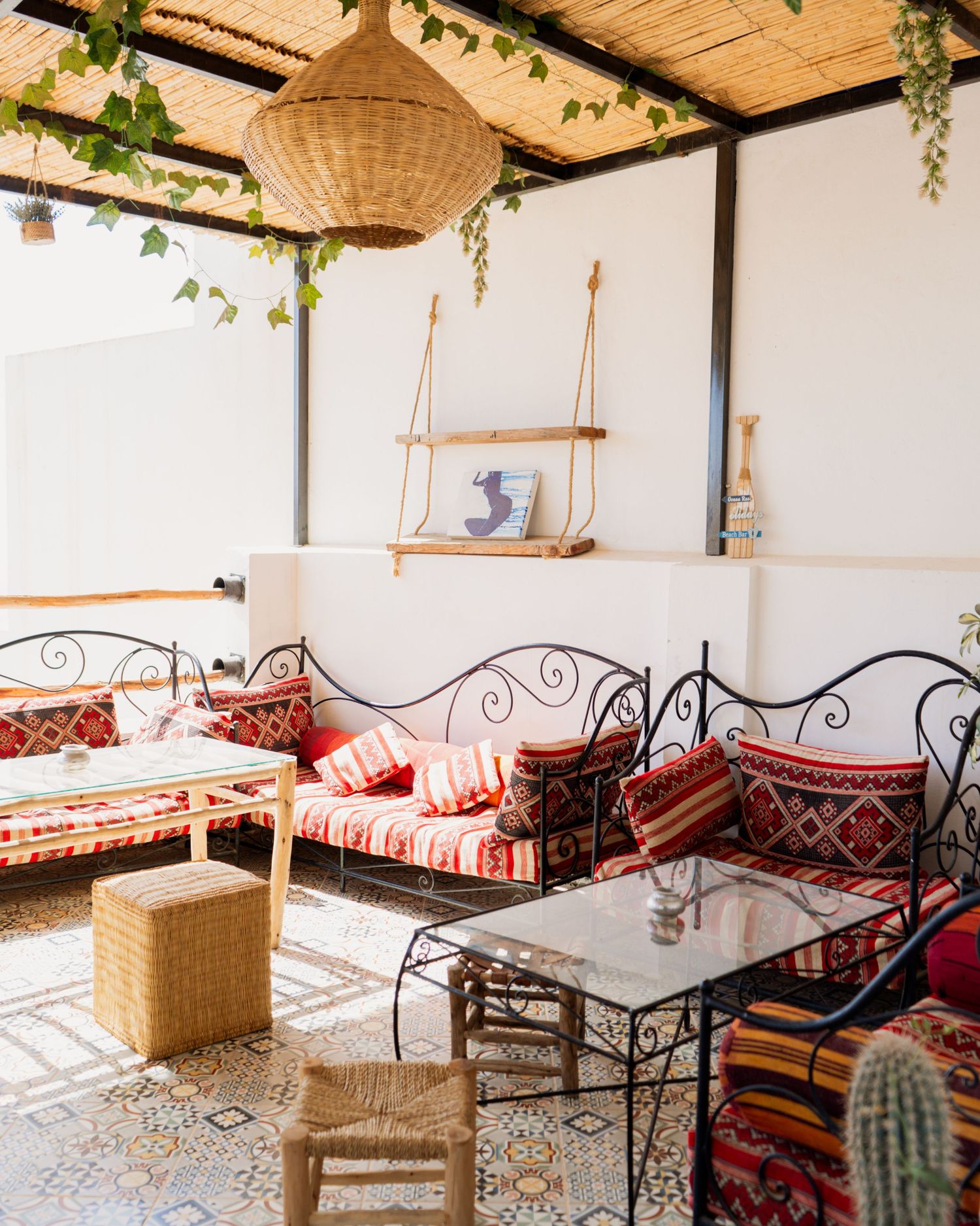 Bohemian outdoor patio with wrought iron sofas, colorful cushions, mosaic tile floors, wicker pendant light, and cactus decor.