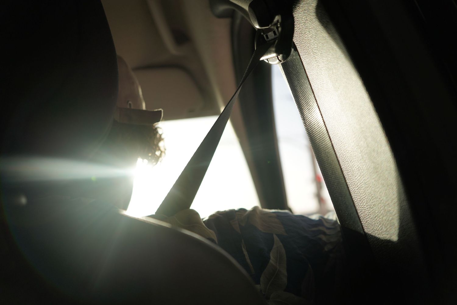 Silhouette of a passenger in a car seat with sunlight streaming through the window and seatbelt visible.