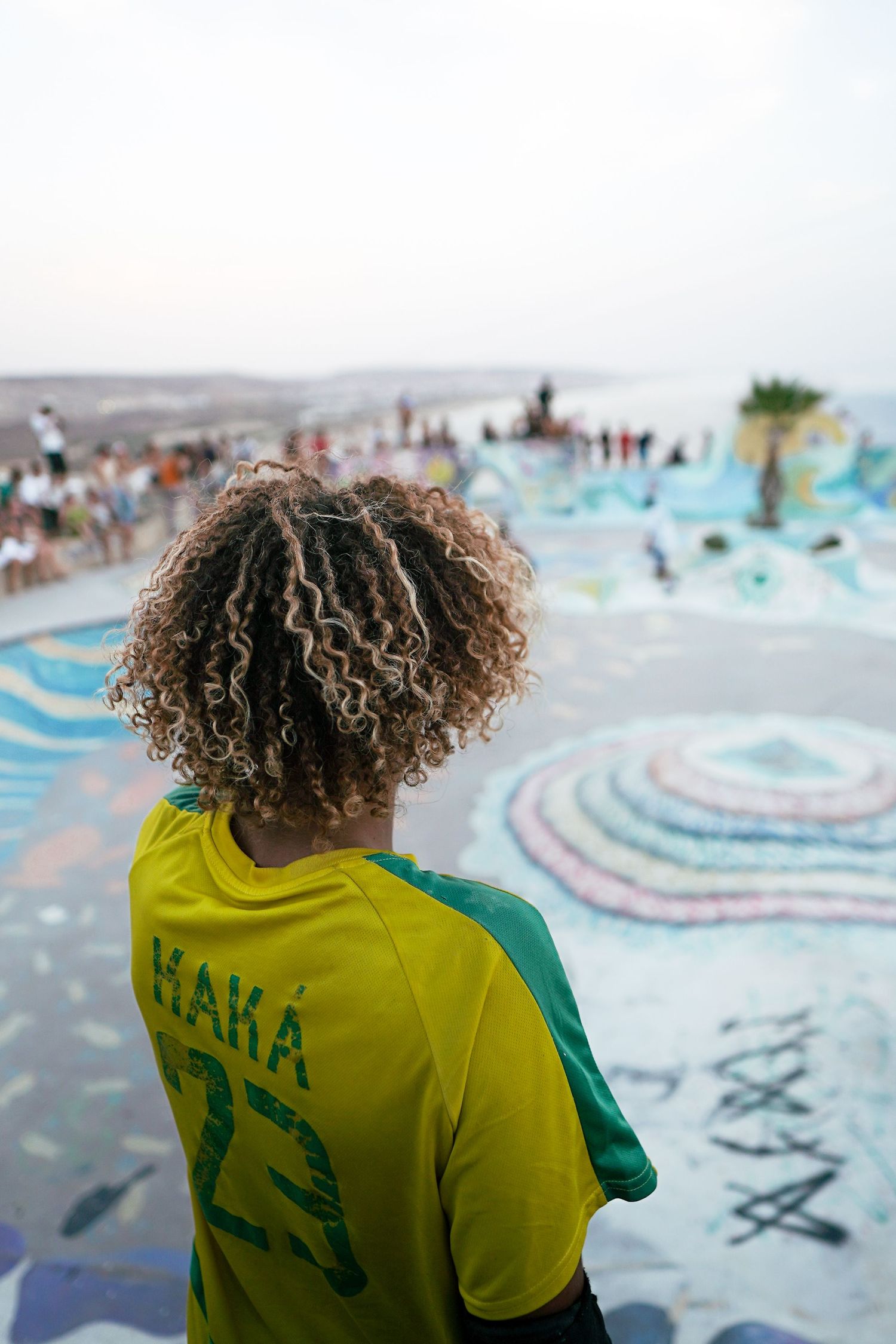 Person with curly hair wearing Brazil Kaka jersey viewed from behind at colorful skate park.