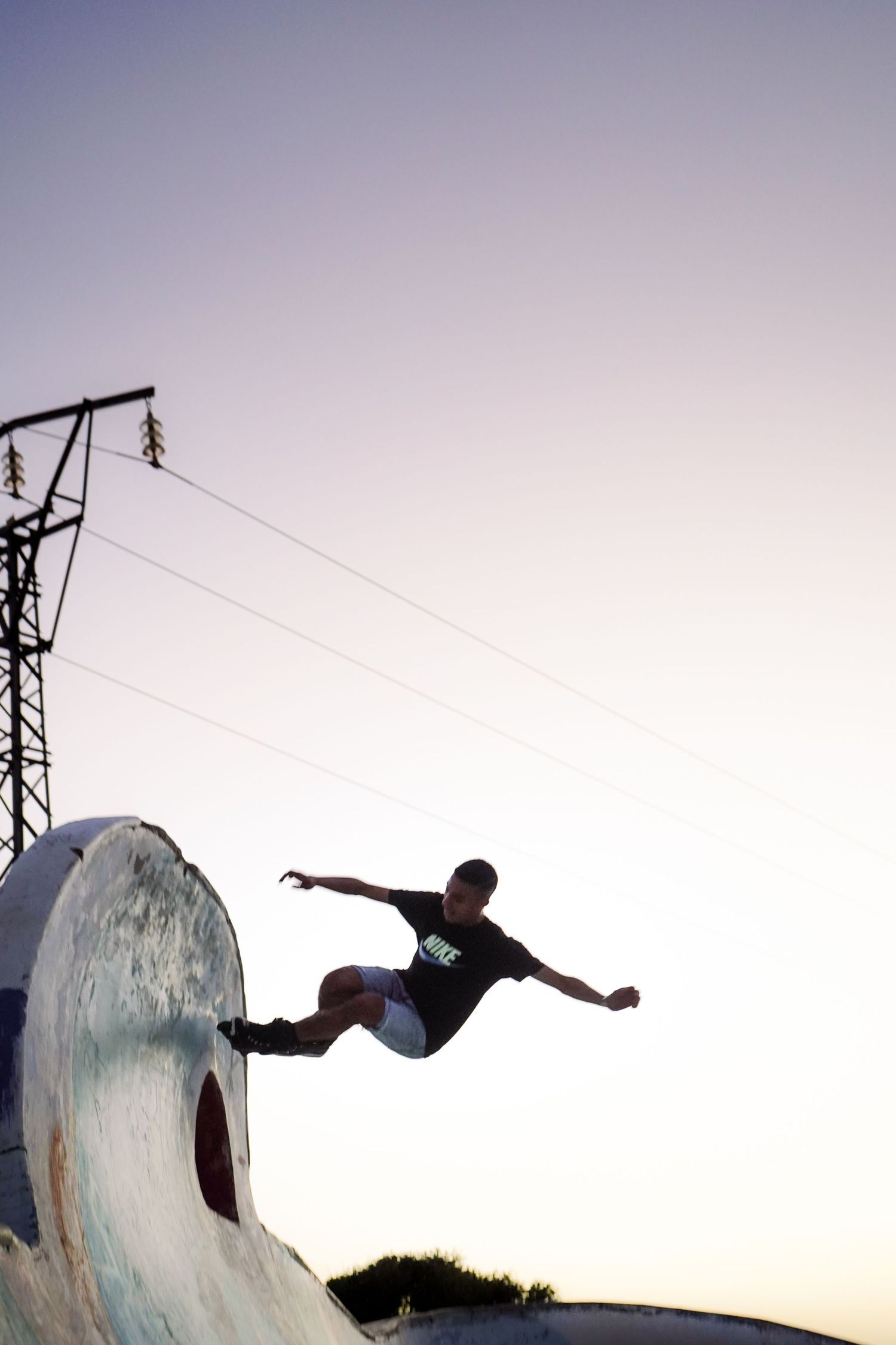 Skateboarder launching off a curved ramp at dusk with power lines and twilight sky in the background.