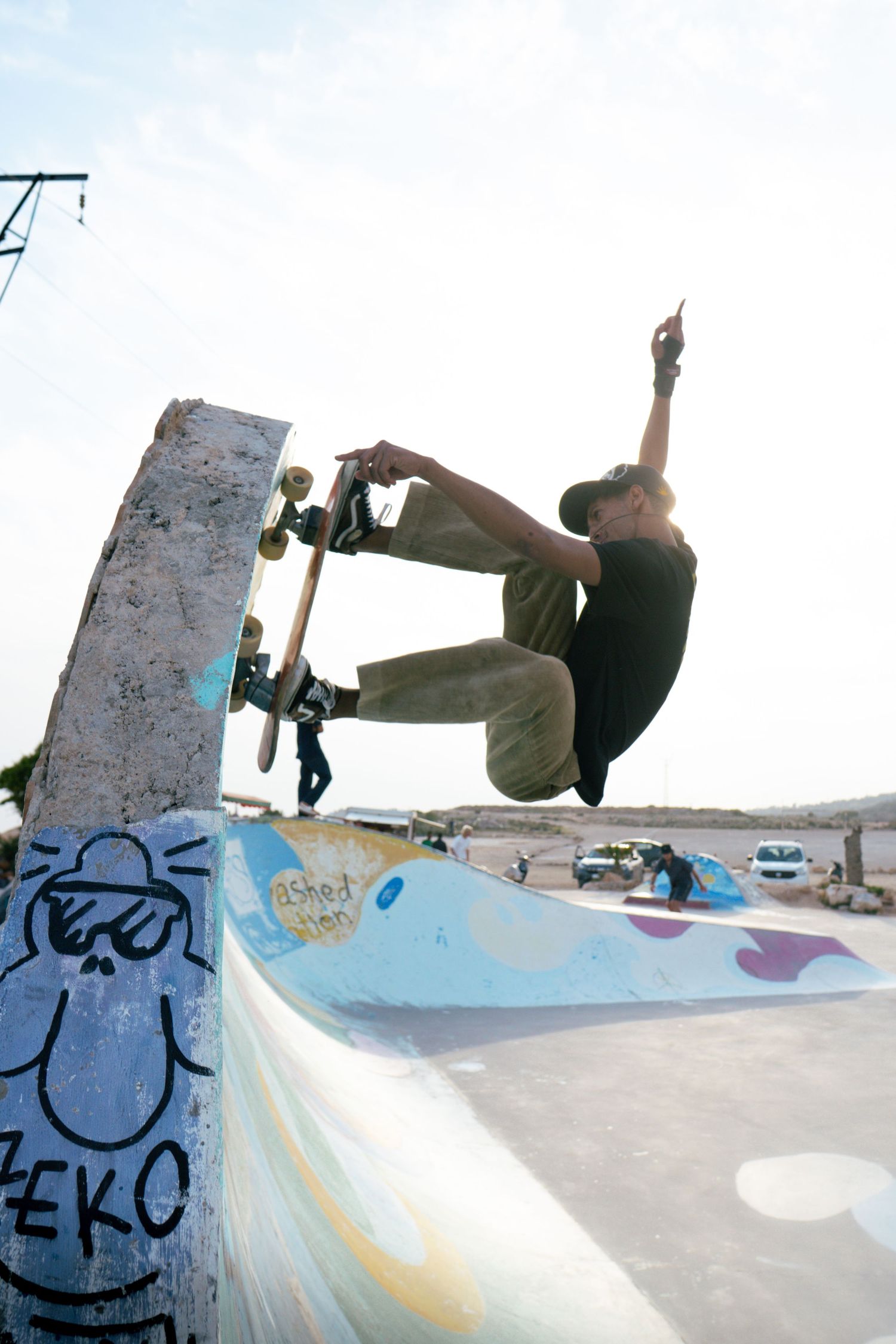 Skateboarder performing aerial trick at graffiti-decorated outdoor skate park during daytime.