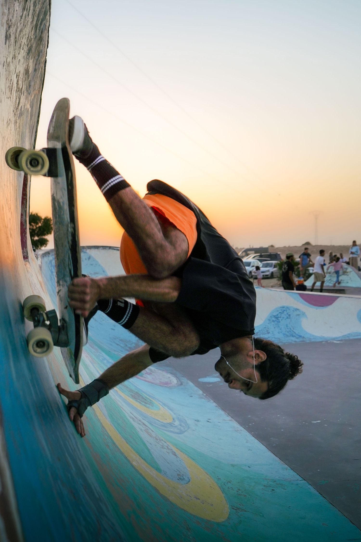Skateboarder performing an inverted handplant trick on a colorful ramp at sunset in an outdoor skate park.