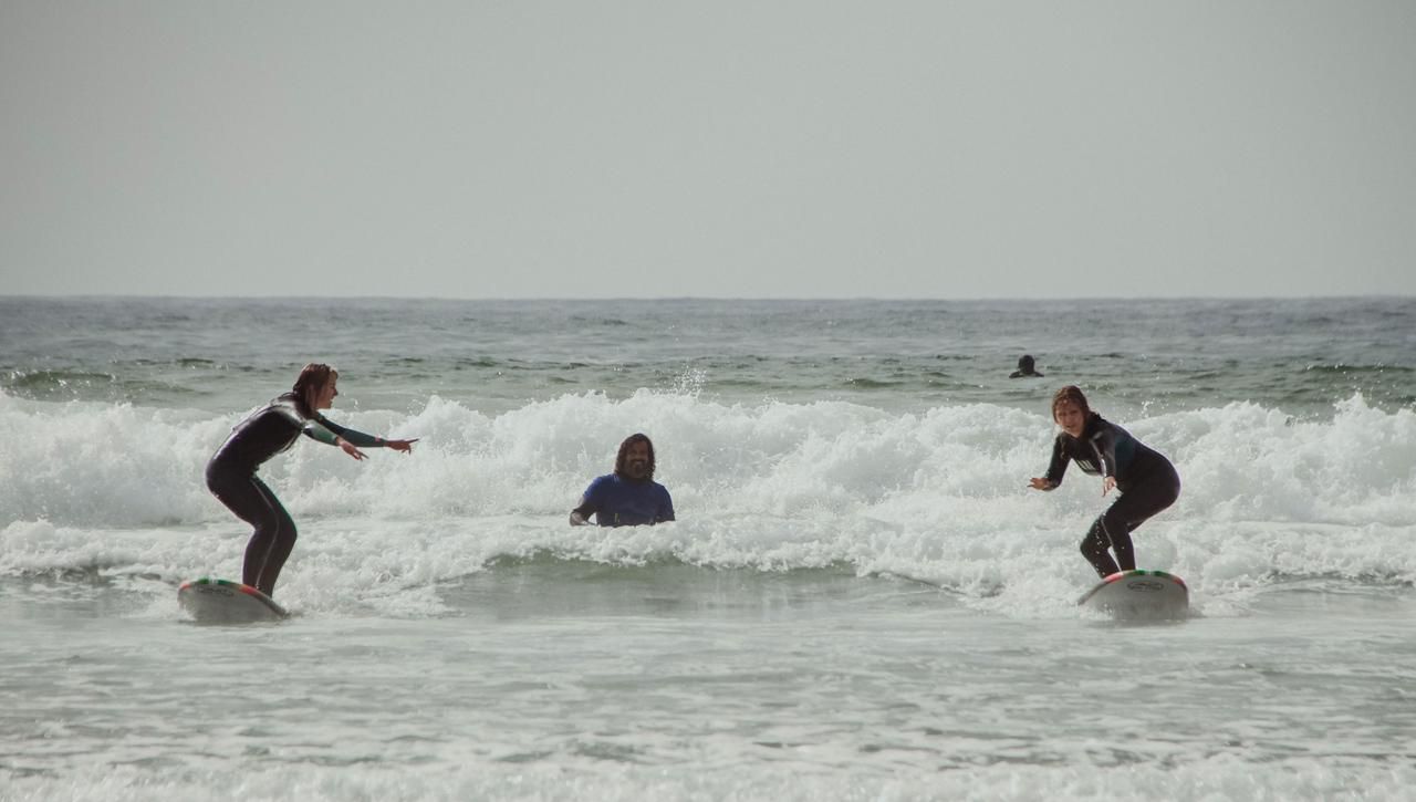 Three surfers in wetsuits ride waves on a cloudy day at the beach, with one person visible in the water between them.