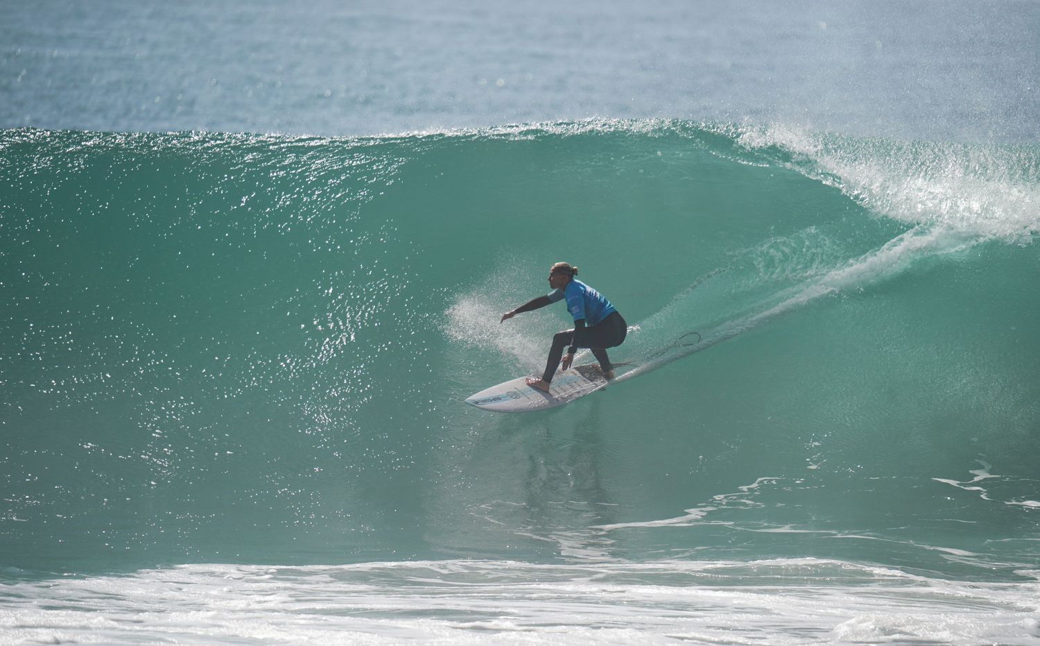 Surfer in a blue wetsuit carving through a large turquoise wave in the ocean.