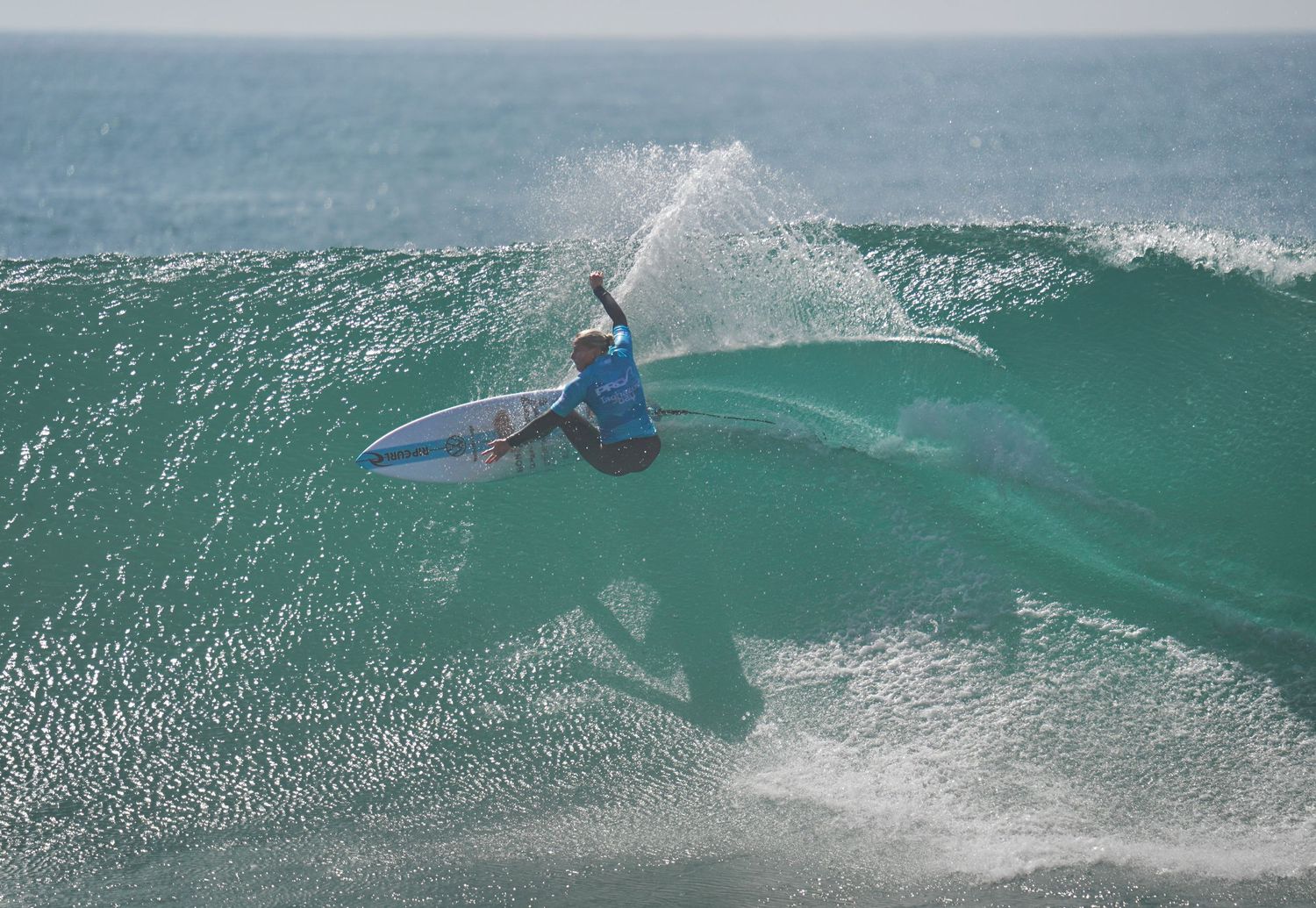 Surfer performing an aggressive cutback maneuver on a large turquoise ocean wave.