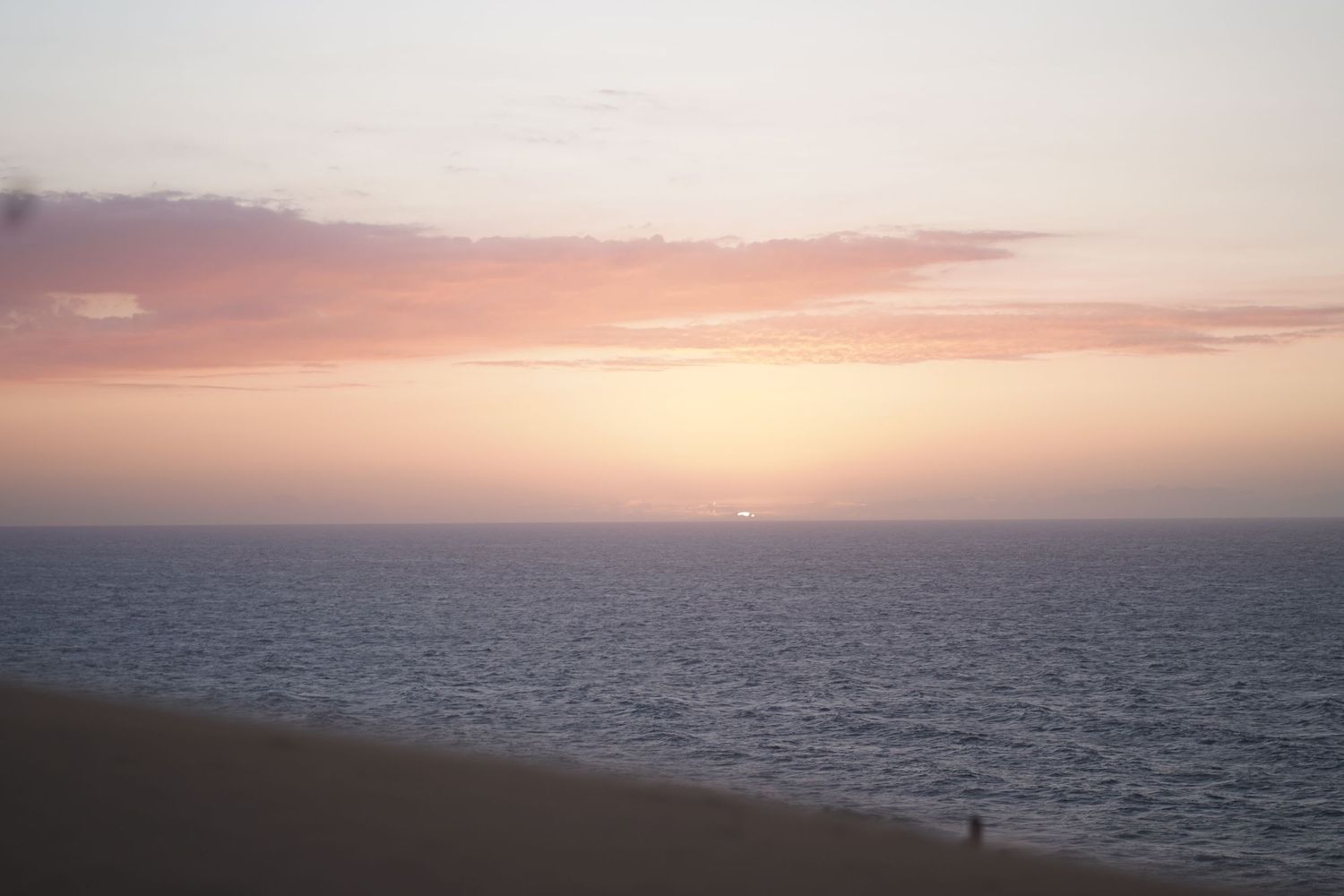 Stunning ocean sunset with pink and orange hues reflecting over calm water and sandy beach.