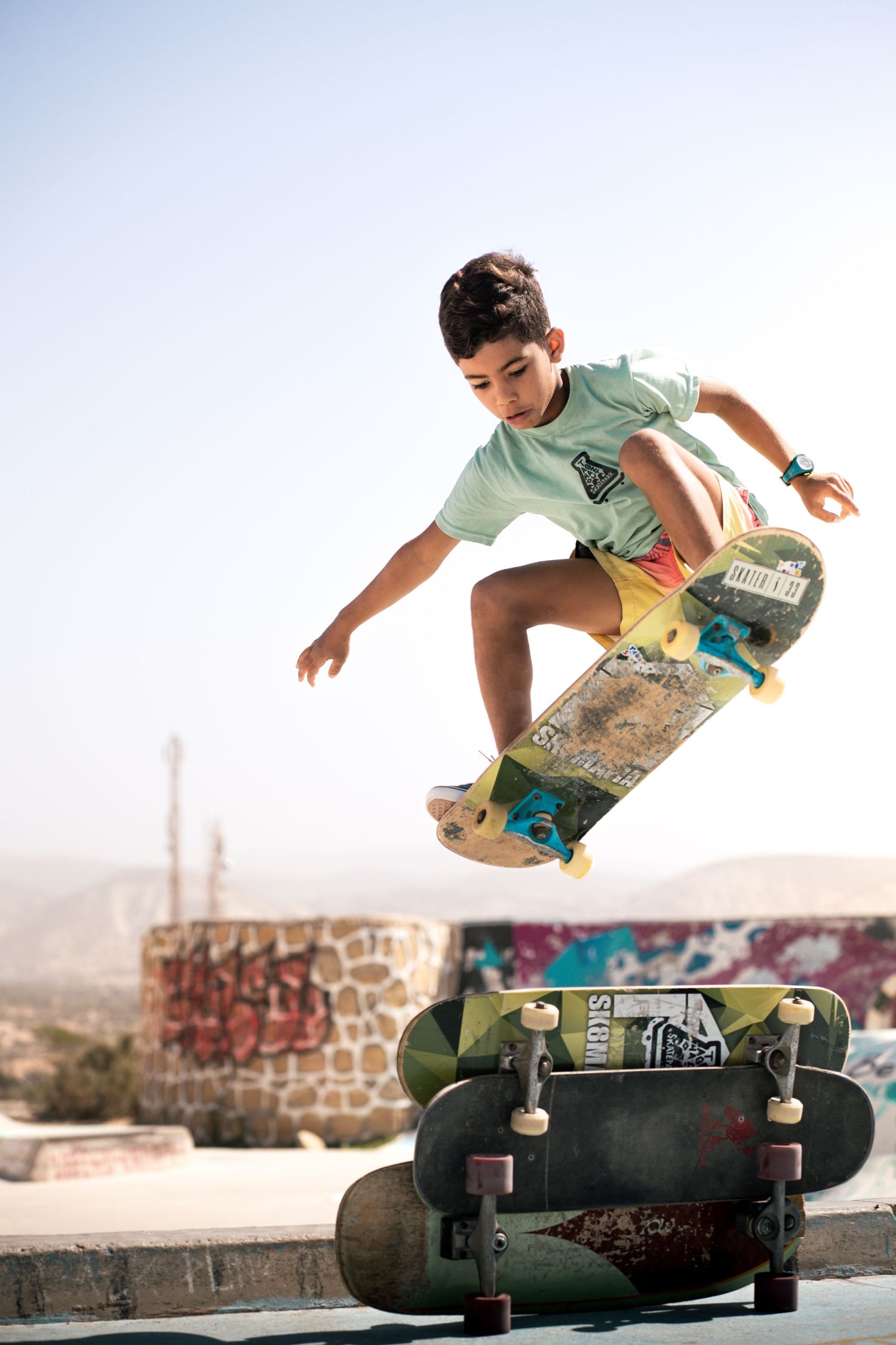 Young skateboarder performing an ollie trick over a skateboard at an outdoor skate park.