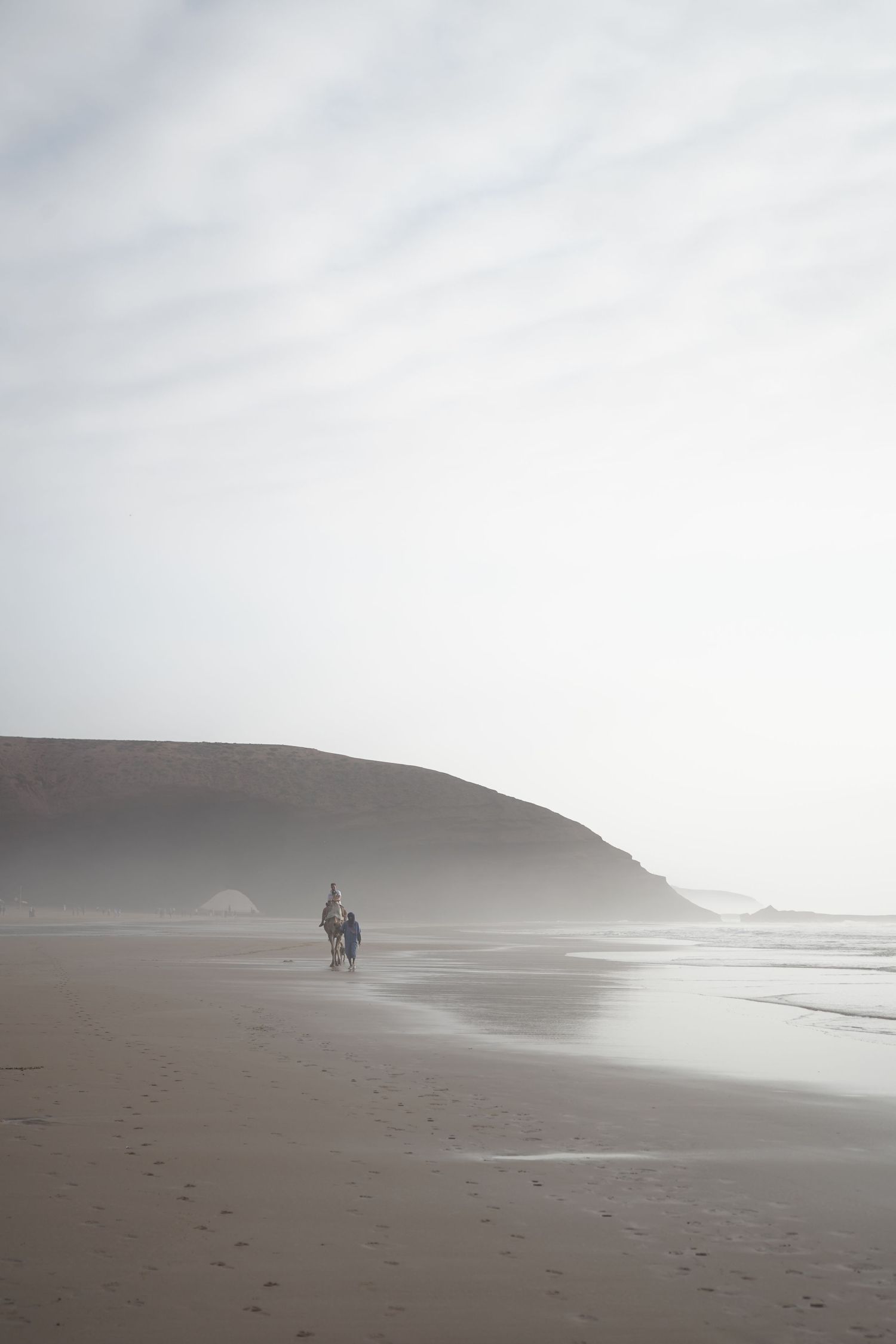 Two people walking on a foggy misty beach with large coastal cliffs in background.
