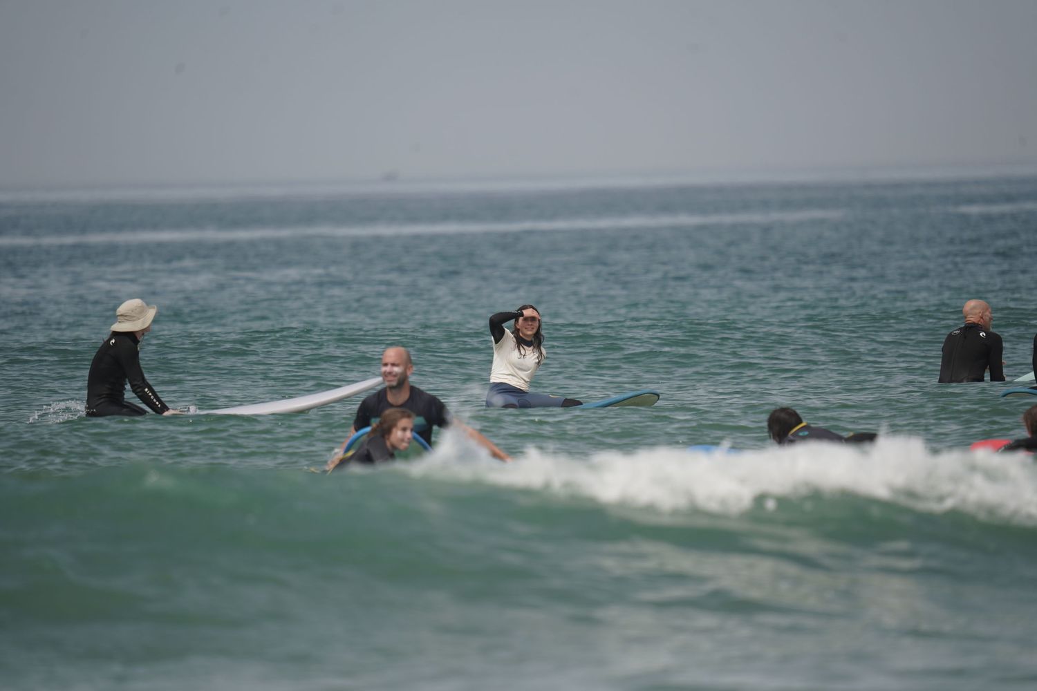 Group of surfers in the ocean on surfboards with one person taking photos amid gentle waves.