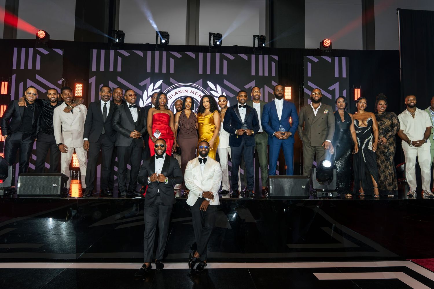 Large group of formally dressed award recipients pose together on a stage at a gala ceremony.
