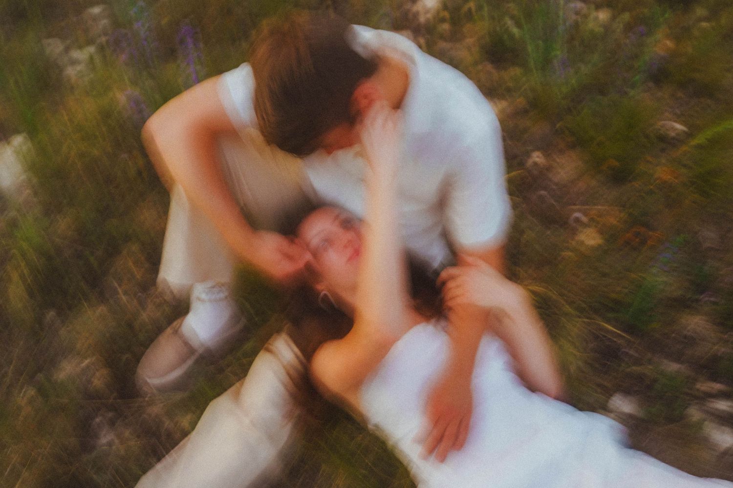 Couple sharing an intimate moment on the grass, captured with a dreamy motion blur effect outdoors.