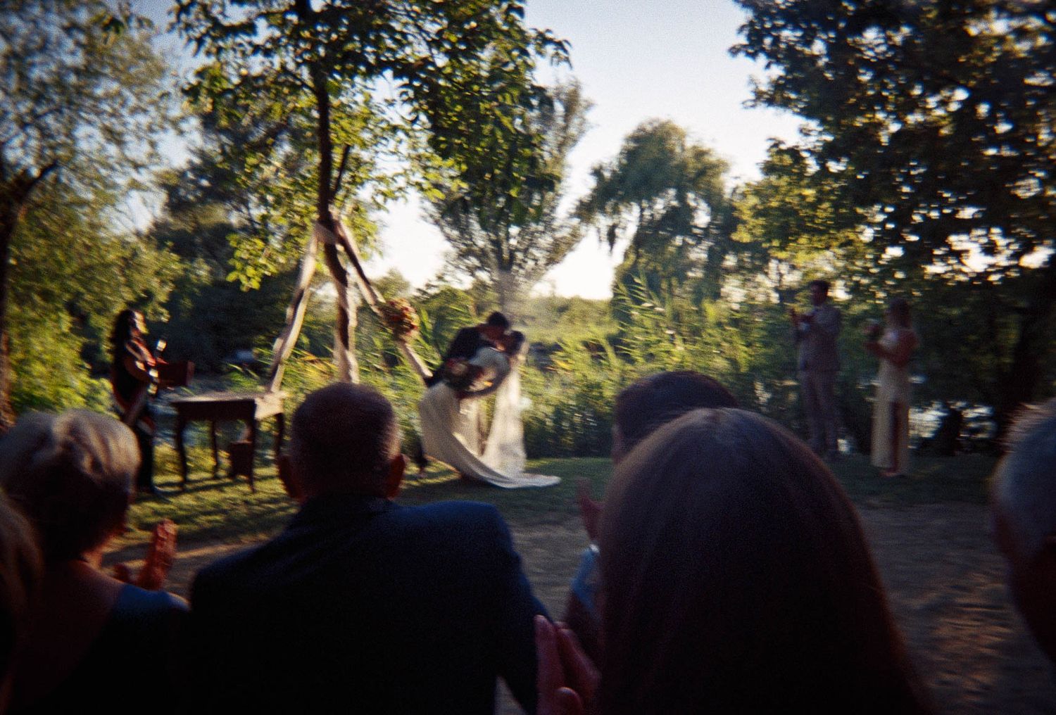 Outdoor wedding ceremony at golden hour with bride and groom silhouetted before seated guests.
