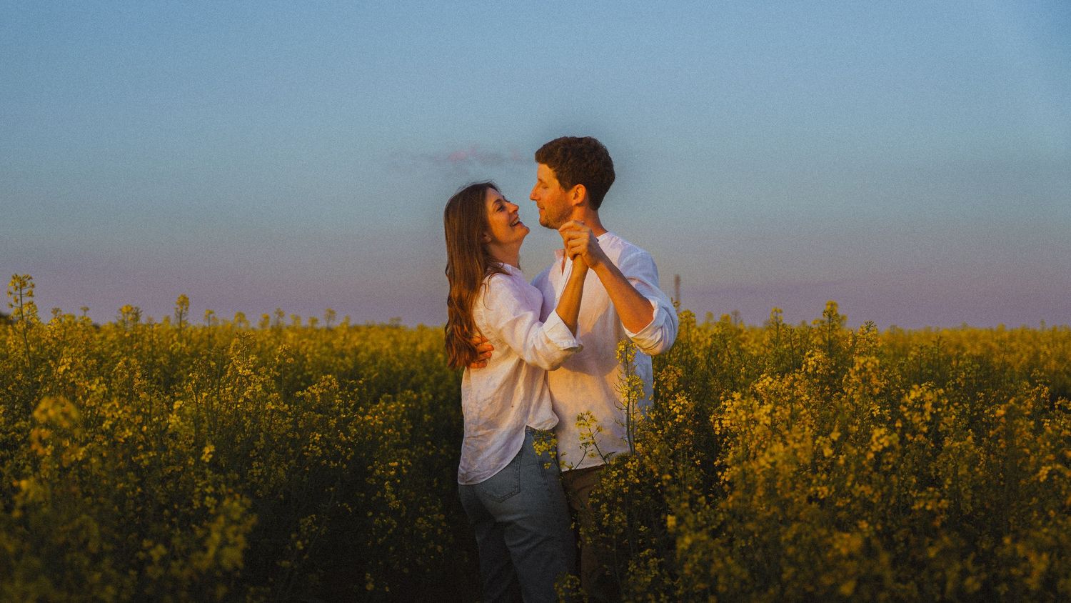 Happy couple dancing and embracing in a yellow flower field at sunset.