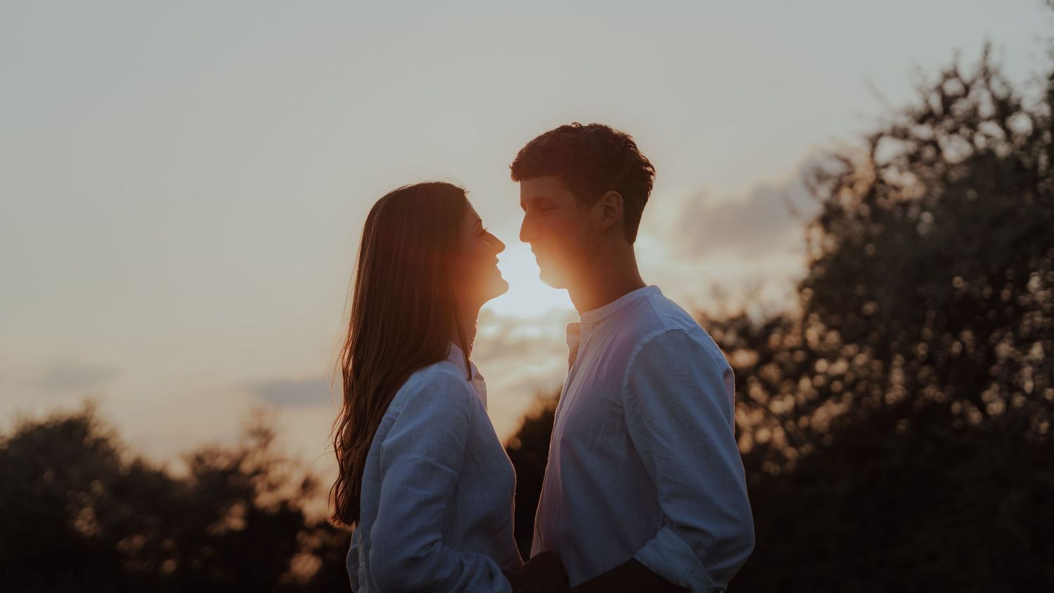 Silhouette of a couple facing each other intimately against a warm sunset sky.