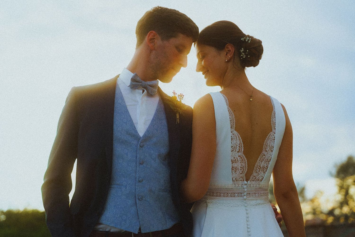 Romantic bride and groom touching foreheads in golden sunset light at their outdoor wedding.