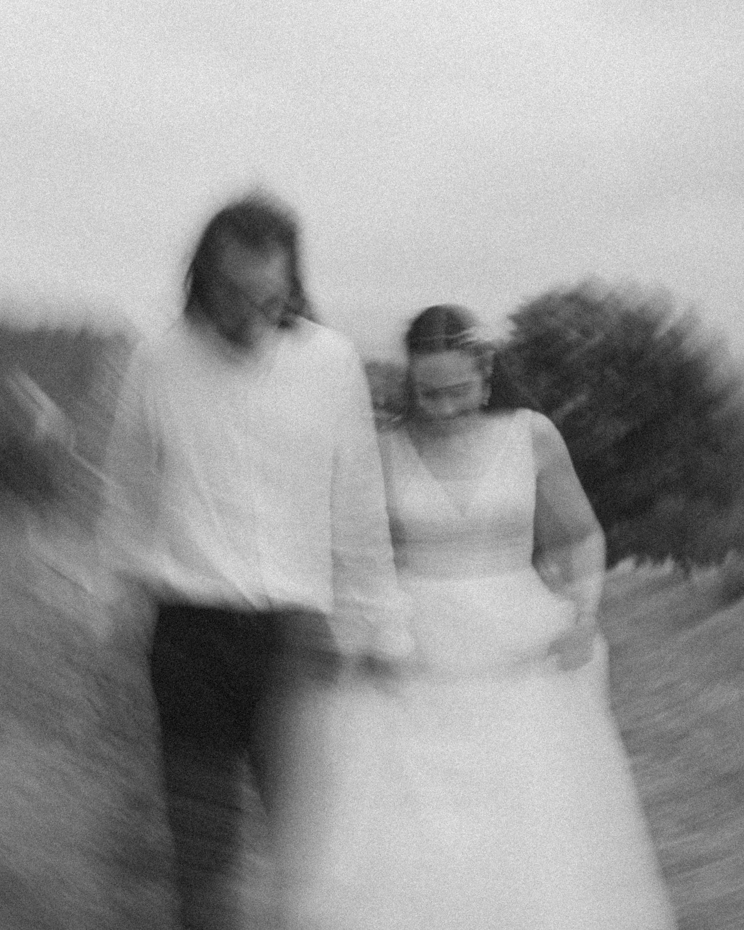 Artistic blurred black and white photo of bride and groom walking together through a field.