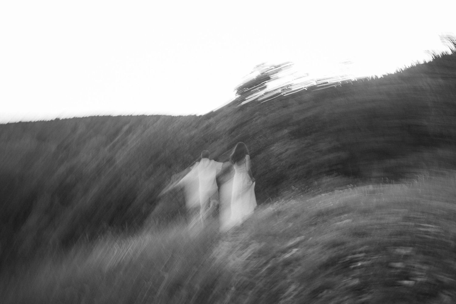 Blurred black and white photo of two people in white dresses running through a field.