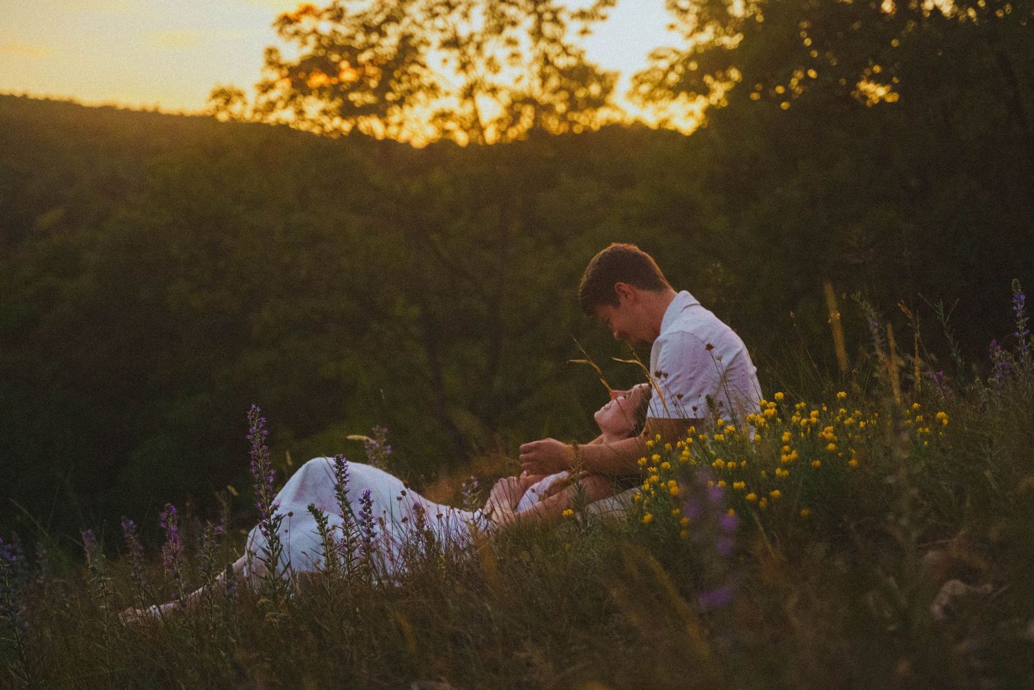 Romantic couple sitting together in a wildflower meadow during a glowing sunset.