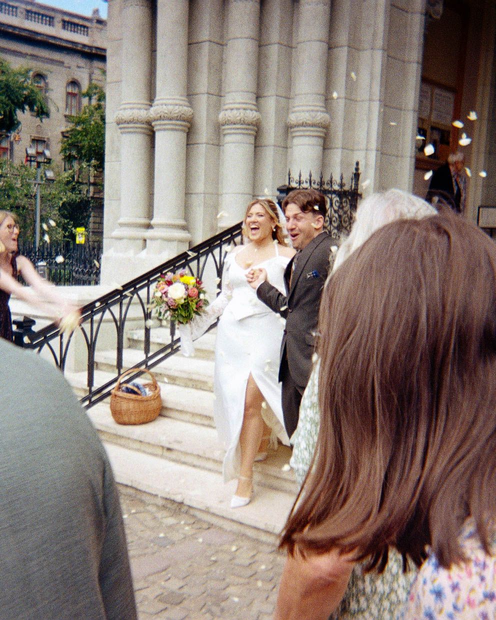 Bride and groom laughing as confetti is thrown on church steps during their outdoor wedding celebration.