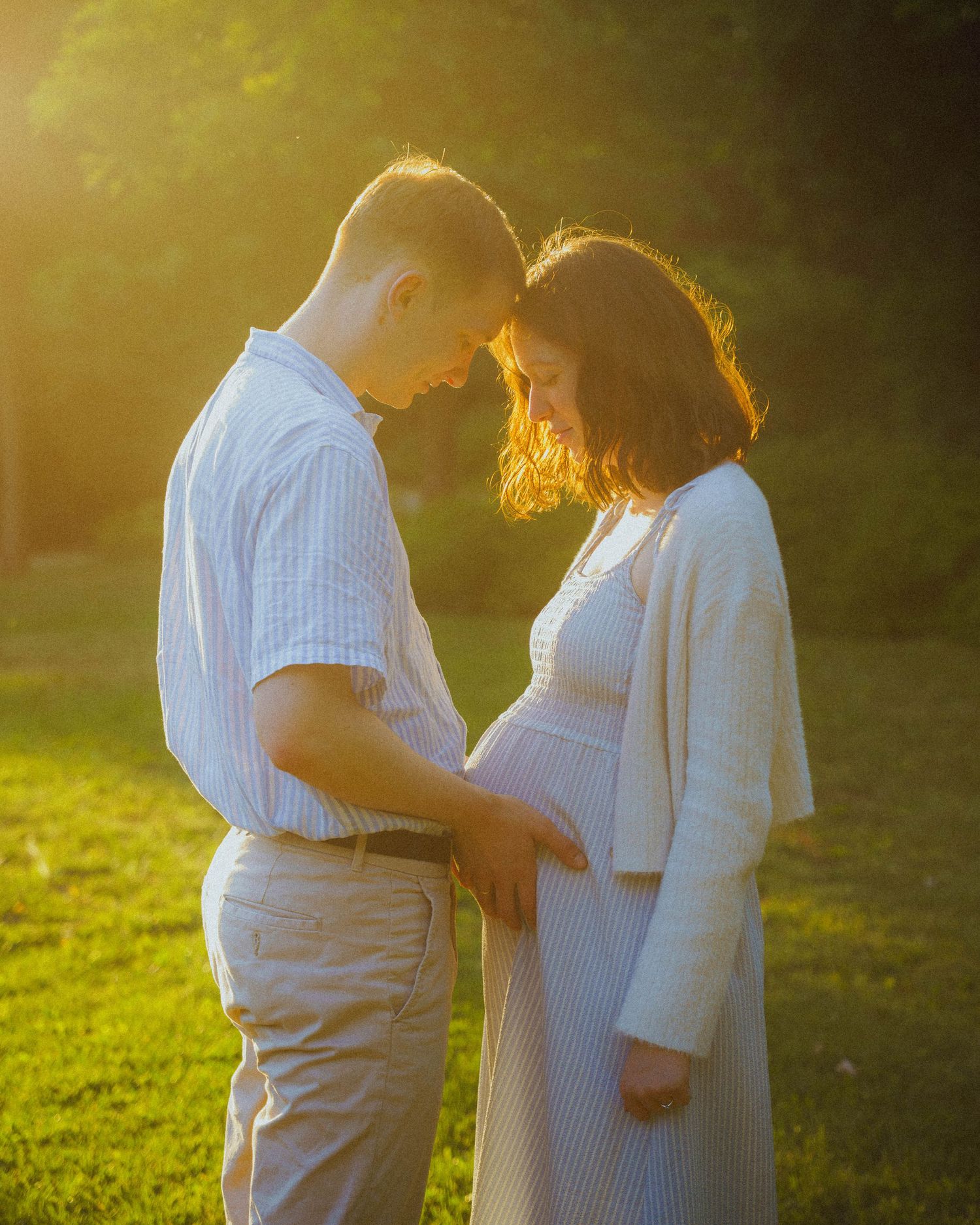 Expecting couple touching baby bump forehead to forehead at sunset.