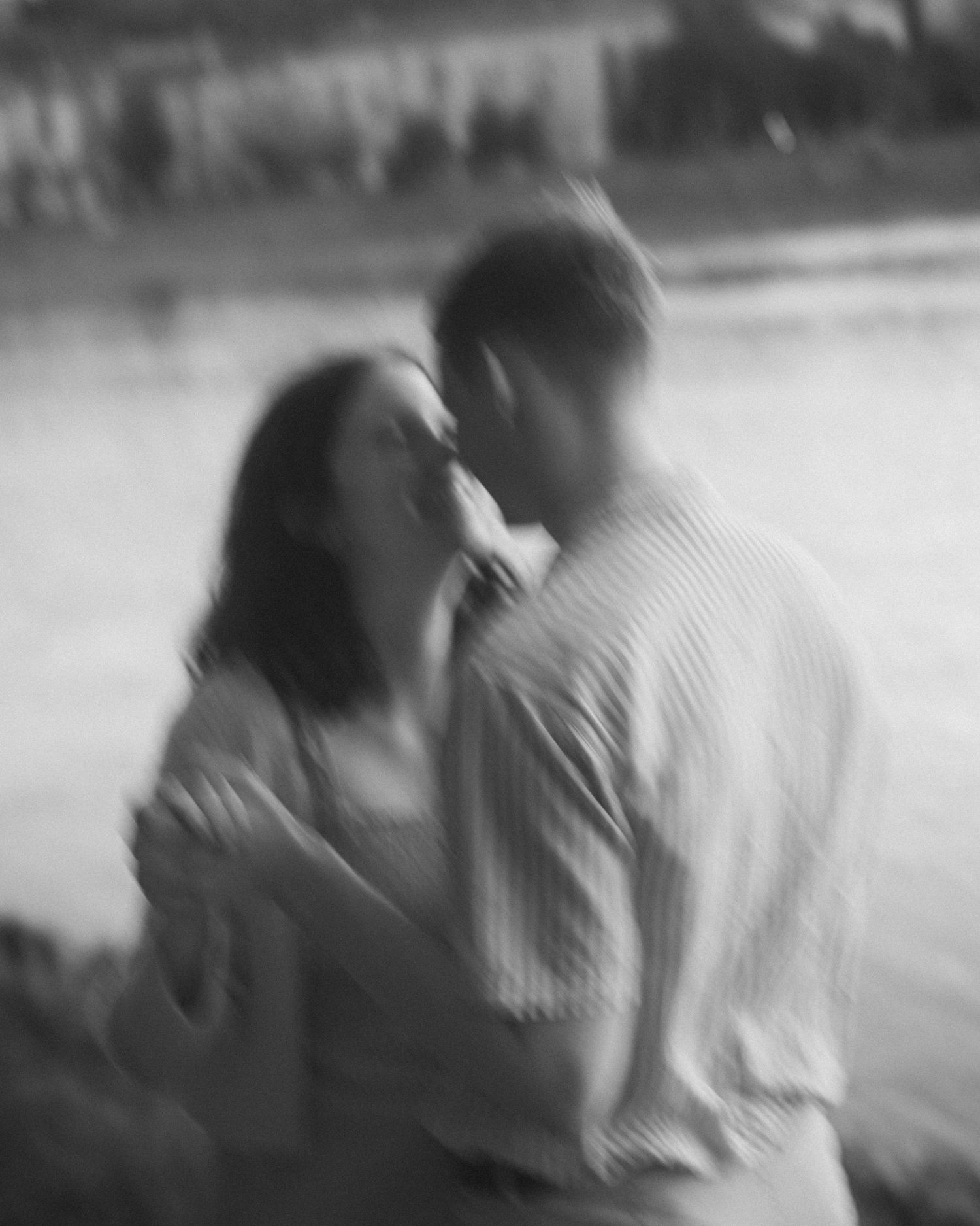 Black and white blurred romantic couple kissing near water.