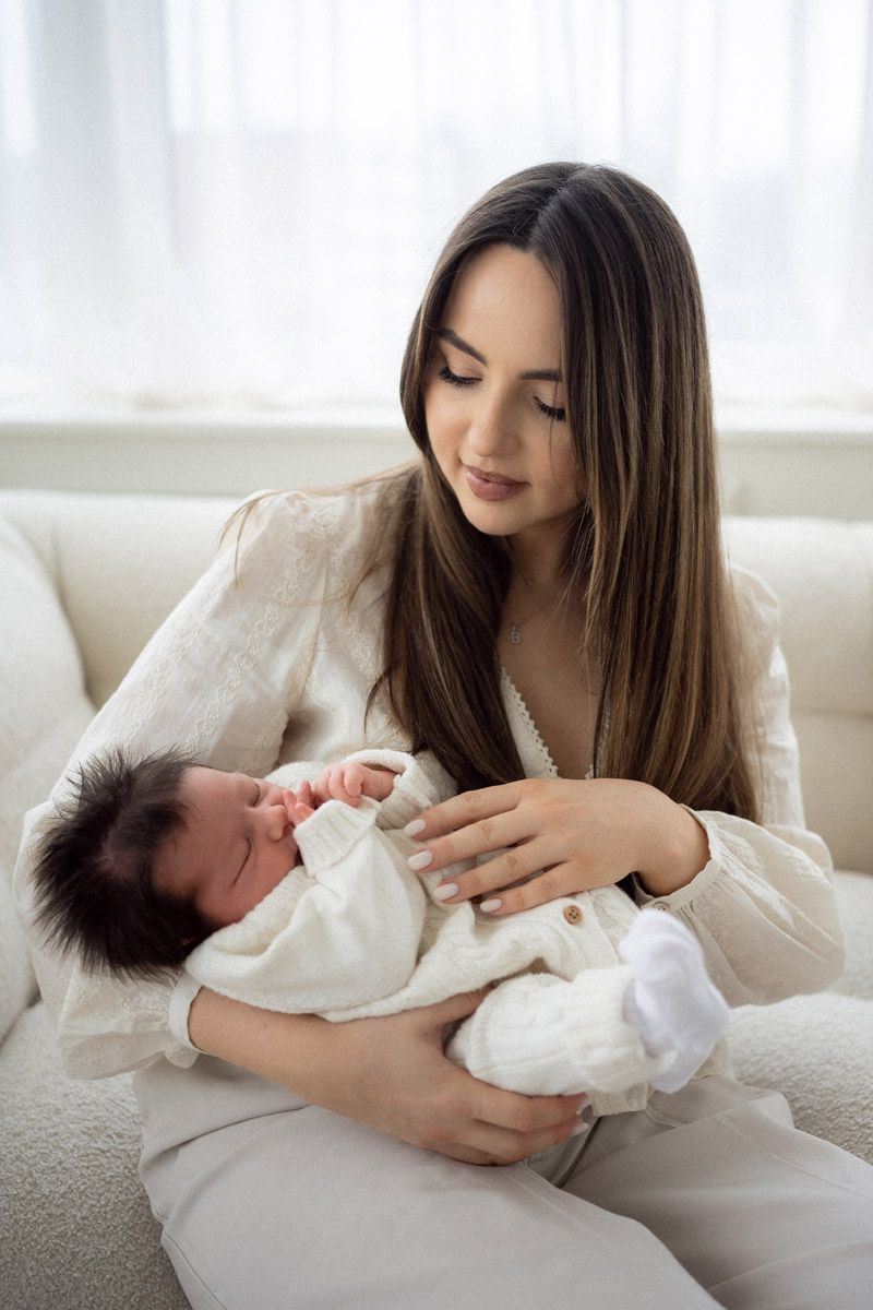 Mother tenderly holding and feeding her newborn baby, close-up studio portrait