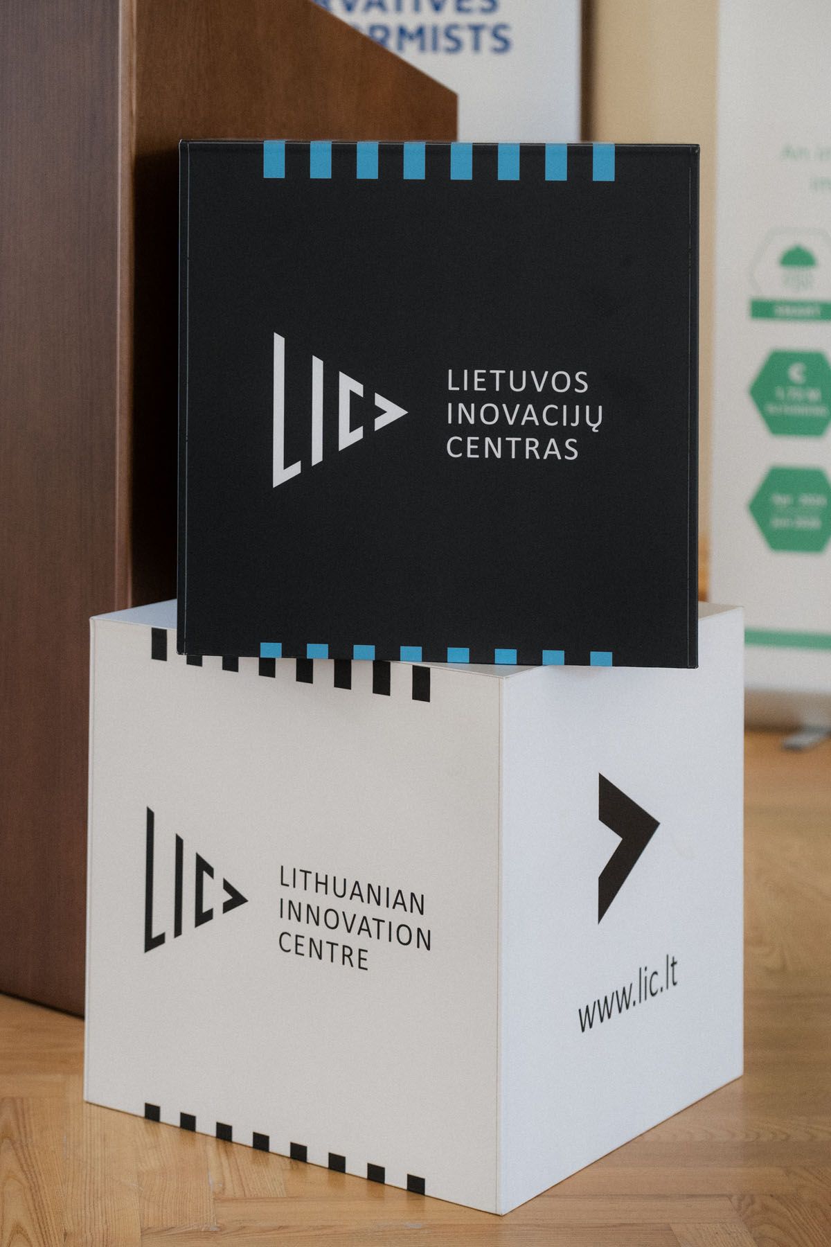 Black and white Lithuanian Innovation Centre logo cubes stacked on a wooden floor at a conference venue.