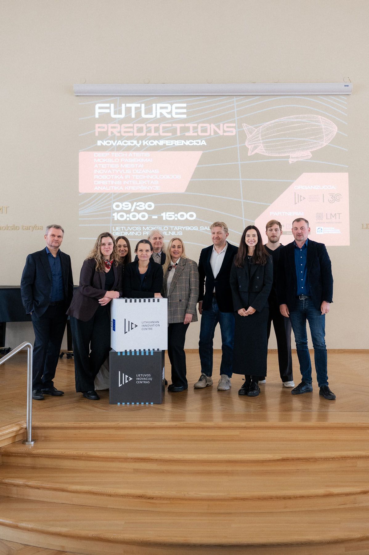 Group of conference participants poses on wooden steps in front of the Future Predictions innovation conference screen.
