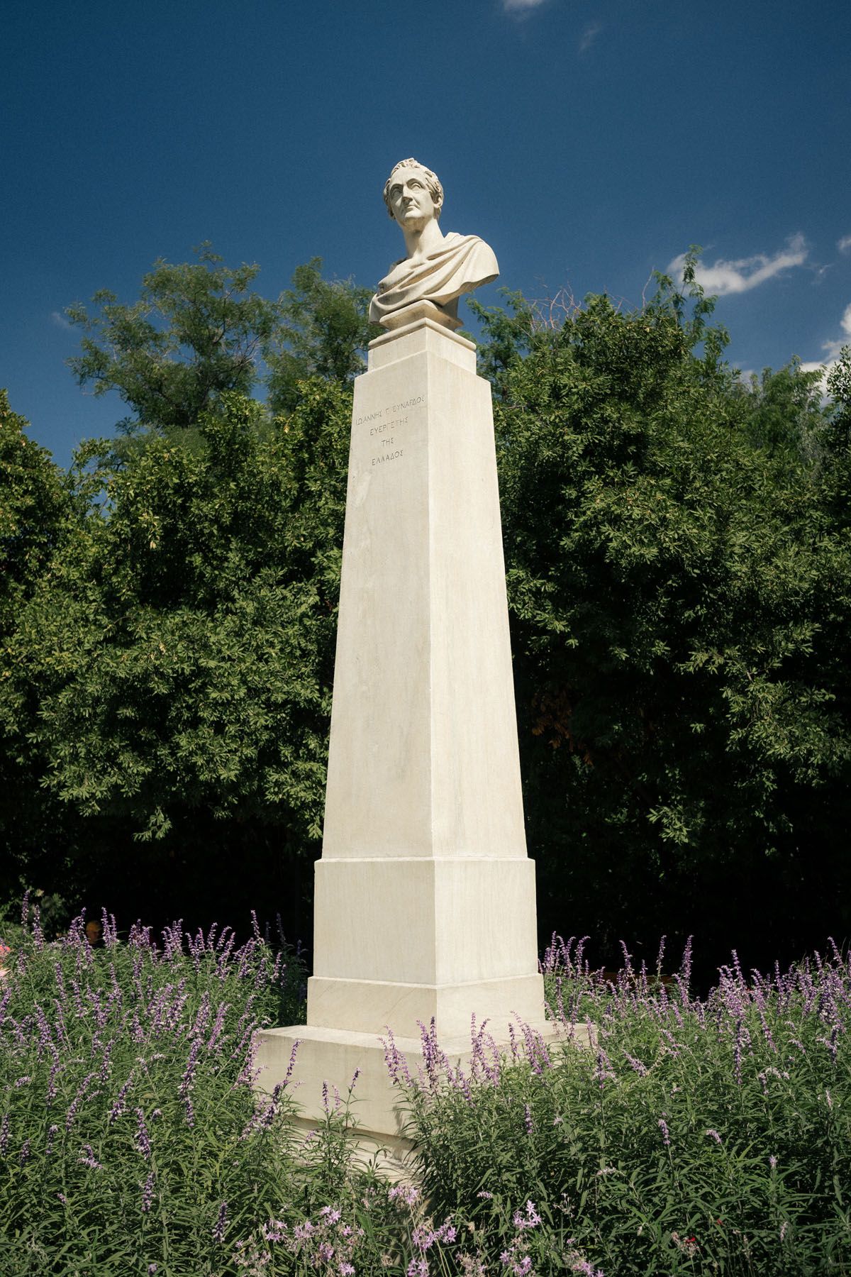 Historic statue in Athens Greece surrounded by trees and blue sky