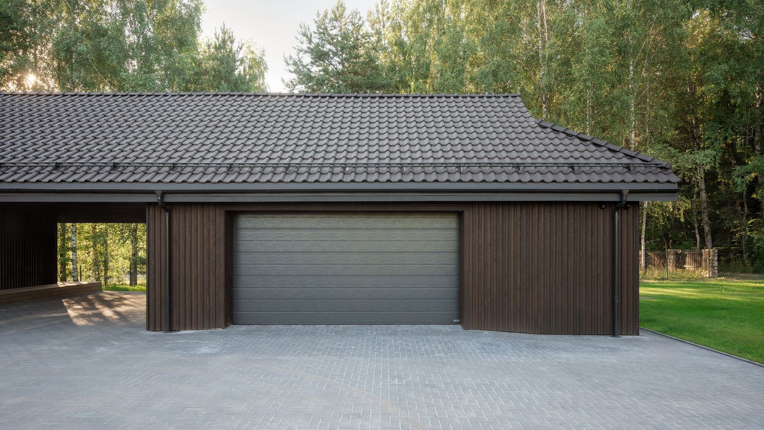 Detached garage with dark timber cladding beside a modern house